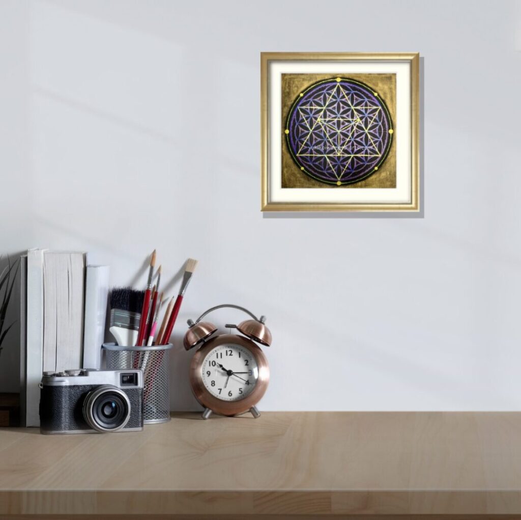 デスク上のカメラや目覚まし時計の横。白い壁に飾られた神聖幾何学アート「宇宙」は、シャンパンゴールド額装で創造力と時間管理をサポート。波動アップを促す手描き原画。