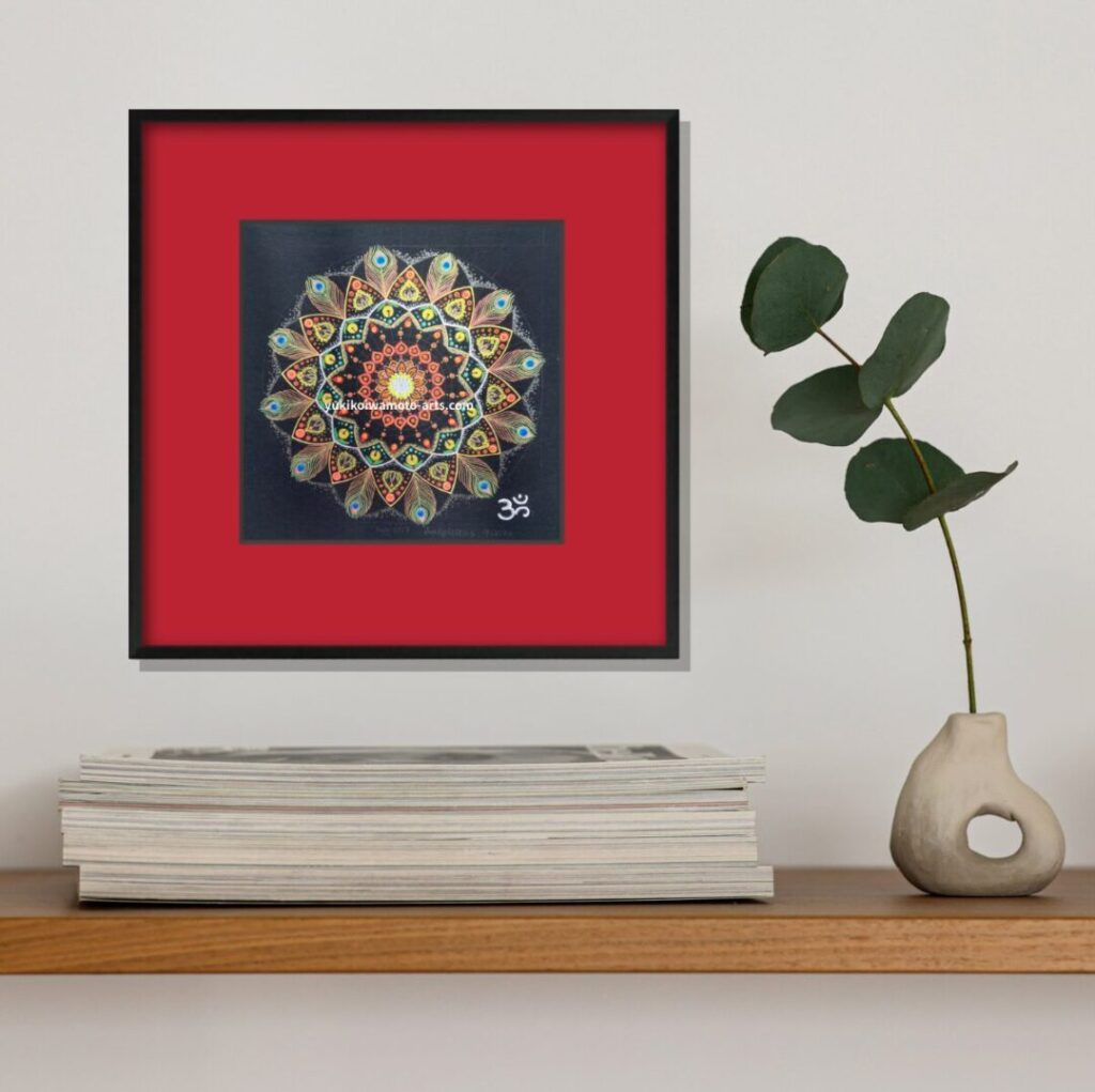 雑誌と一輪挿しの横に飾られた赤いマットの曼荼羅アート「吉兆」。日常の読書空間に彩りを添える。