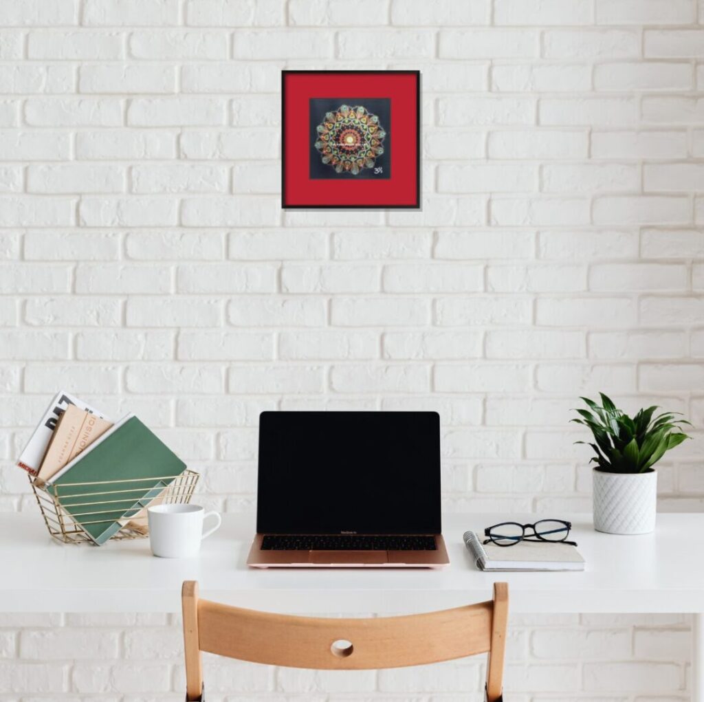 オフィスの白い壁、パソコンの上に飾られた曼荼羅「吉兆」。事業成功への意図を込めた配置。